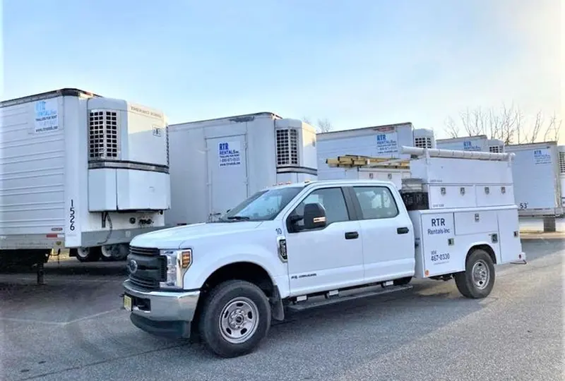 image_quad White utility truck parked near refrigerated trailers.